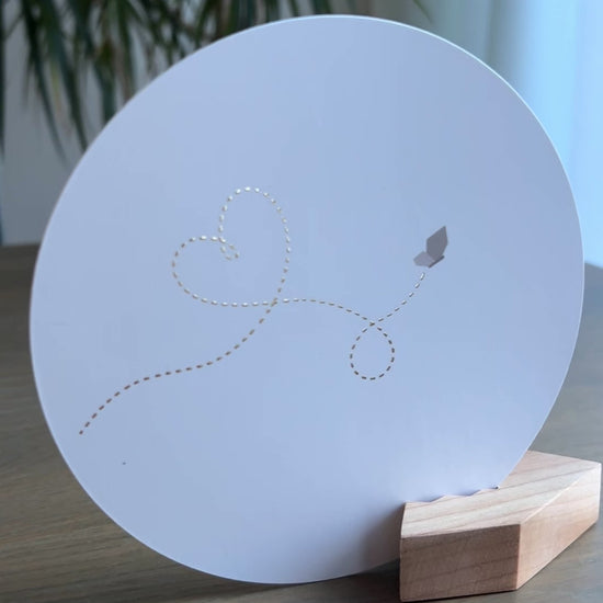 Witte ronde wenskaart in een houten blokje met een vlinder die een gouden stippellijn met een hartje fladdert