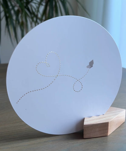 Witte ronde wenskaart in een houten blokje met een vlinder die een gouden stippellijn met een hartje fladdert